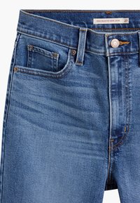 Jean mom taille haute bleu avec bouton et fermeture éclair à l'avant, poche avant visible et petite poche à monnaie avec couture orange.