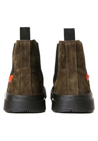 Stivaletti in suede marrone con pannelli laterali elastici neri, dotati di una suola in gomma testurizzata e un'accensione rossa sul lato.