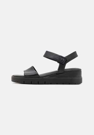 Black leather sandals with a wide strap across the toe and adjustable slingback. Features a thick, textured sole with grooves.