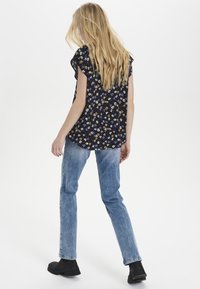 Námořnický top s květinovým vzorem a volánkovými rukávy, kombinovaný se světle modrými rovnými džíny a černými kotníkovými botami. Jednoduchý design, neformální vzhled.