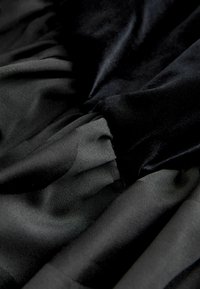 Czarna tkanina z gładkimi i teksturowanymi warstwami, z mieszanką matowych i błyszczących powierzchni w marszczonym wzorze. Miły i lekkawy wygląd.