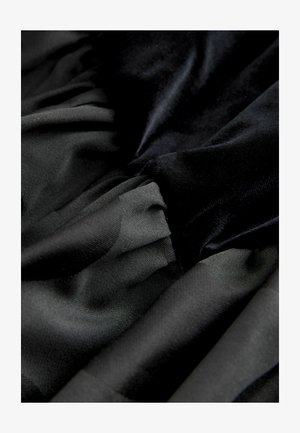 Schwarzer Stoff mit glatten und strukturierten Schichten, der eine Mischung aus matten und glänzenden Oberflächen in einem gerafften Design aufweist. Weiche und fließende Erscheinung.
