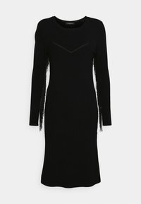 Robe noire en tricot avec manches longues et détails à franges le long des bras. Elle présente un col rond et une silhouette ajustée.