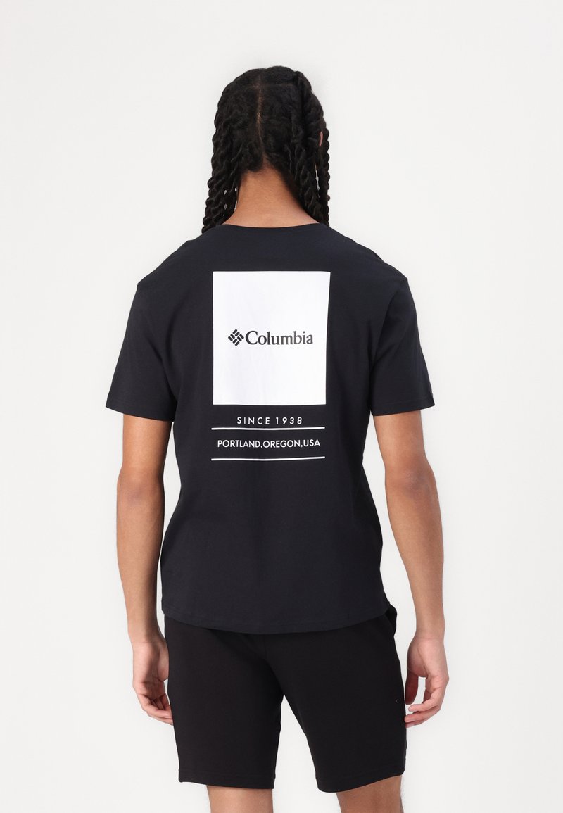 Sort kortærmet t-shirt med et hvidt rektangulært grafisk design med "Columbia" og tekst nedenfor, parret med sorte shorts.