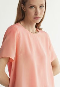 Ljusrosa kortärmad blus med rund halsringning. Slätt, lätt tyg med avslappnad passform och minimalistisk design.