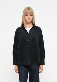 Czarna koszula z guzikami, z kołnierzykiem, długimi rękawami i luźnym krojem. Wykonana z teksturowanej tkaniny, z metalowymi guzikami i zaokrąglonym hemem.
