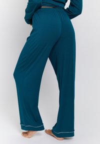 Teal, wide-leg lounge pants made from soft fabric. Features an elastic waistband and white trim at the hem. Plain texture, relaxed fit.