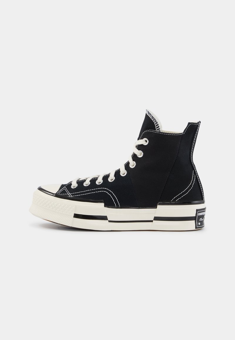 Baskets montantes en toile noire avec lacets blancs, semelle en caoutchouc blanche avec rayures noires et patch de talon marqué, vues de côté sur fond blanc.