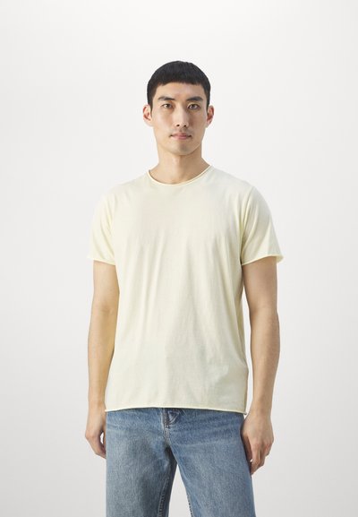 T-shirt en coton jaune clair à manches courtes et col rond, porté avec un jean en denim bleu, présenté sur fond blanc.