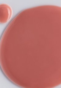 Liquido rosa con una finitura lucida, steso in forma circolare, con una goccia più piccola accanto su sfondo bianco.