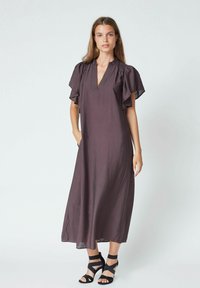 Rochie lungă de culoare prune, cu mâneci tip flutter și decolteu în V, fabricată dintr-un material ușor. Modelul poartă sandale negre cu bretele.