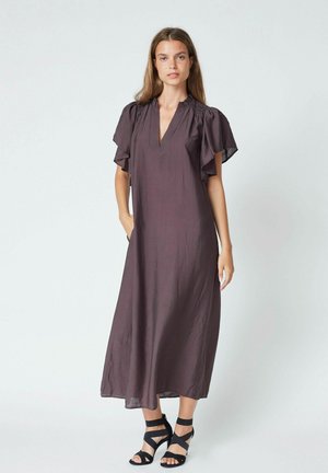 Abito lungo di color prugna con maniche a volant e scollatura a V, realizzato in un tessuto leggero. La modella indossa scarpe con tacco nere a strappo.