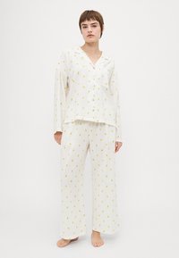 Lightweight white pajama set in ribbed texture, featuring a button-up top and loose pants, adorned with small yellow floral patterns.