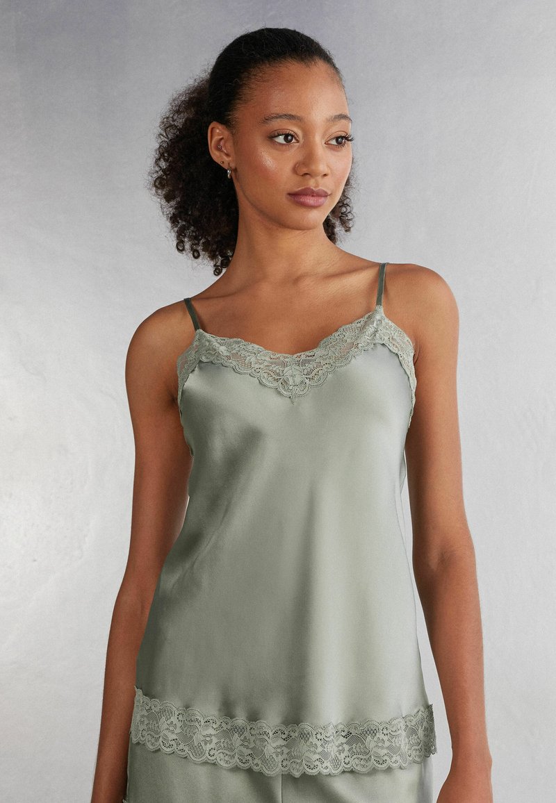 Satin topje in gedempt groen met spaghettibandjes, voorzien van kant langs de halslijn en zoom, gladde textuur met een subtiele glans.