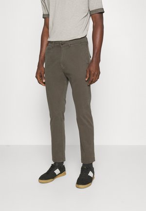 Tummanoliivinvihreät kevyet chinos-kangashousut slim fit -mallissa, joissa on etutaskut ja nappisulku, yhdistettynä mustiin ja valkoisiin lenkkareihin.