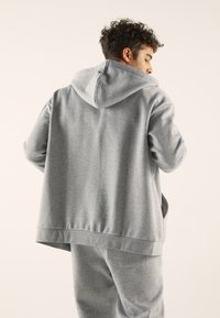 Gray hooded sweatshirt in soft fabric with a kangaroo pocket and relaxed fit, featuring ribbed cuffs and hem. Smooth texture, casual design.