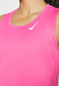 Detailní záběr na osobu v jasně růžovém bezrukávovém sportovním topu Nike s bílým logem Nike na hrudi.