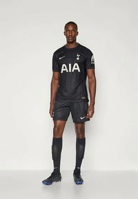 Juodas futbolo kostiumas, turintis tekstūruotą marškinėlį su "AIA" baltu užrašu, suderinami šortai, kojinės ir juodi sportbačiai su mėlynais akcentais.