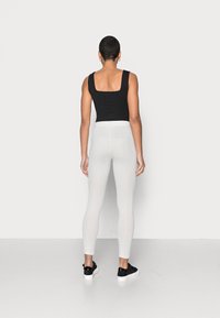 Top preto de alças com decote quadrado combinado com leggings brancas texturizadas. Modelo usa ténis pretos. Silhueta simples e ajustada.