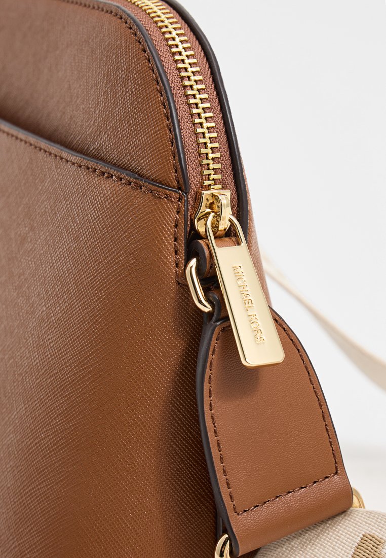 Gros plan sur le coin d'un sac en cuir texturé marron avec une fermeture éclair dorée et un tirette de fermeture éclair de marque Michael Kors.