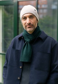 Marine uldblandingsjakke med to forlommer, grå sweater under, grøn strikket tørklæde og lysegrå hue. Udendørs miljø.
