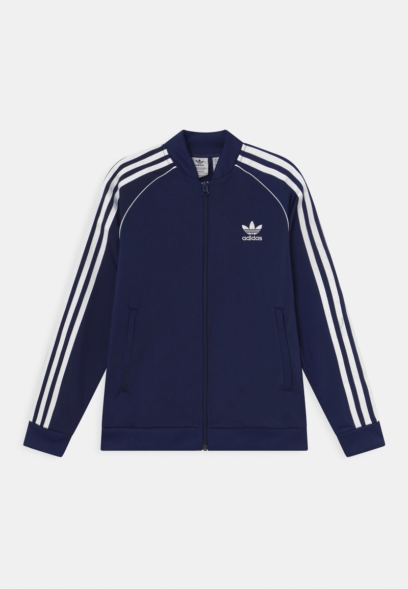 Veste de survêtement Adidas bleu marine avec des rayures blanches sur les manches, fermeture éclair à l'avant, col montant et logo Adidas sur la poitrine gauche.