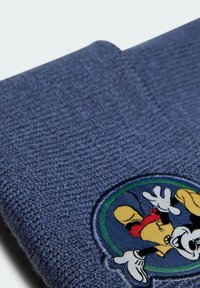Cappello di lana blu con un patch ricamato circolare che presenta personaggi dei cartoni animati. La texture è a coste, con una finitura morbida.