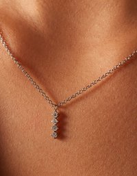 Collar de plata esterlina con una cadena delicada y cuatro piedras similares a diamantes alineadas verticalmente de diferentes tamaños sobre un fondo de piel texturizada.