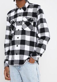 Svart och vit rutad flanellskjorta med två bröstfickor, knapplåsning och långärmade ärmar, som bärs med ljusblå denimjeans.