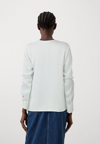 Bluză cu mâneci lungi, de culoare verde deschis, cu o textură fină, decolteu rotund și detalii contrastante negre, asortată cu o fustă din denim.