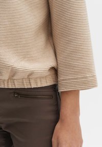 Beige striped sweater with a textured finish and a gathered hem, paired with dark brown pants featuring a zippered pocket.
