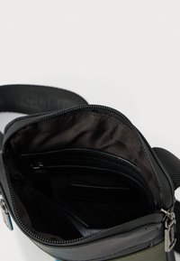 Μαύρο τσαντάκι χιαστί με λείο εξωτερικό, κλείσιμο με φερμουάρ και ευρύχωρο εσωτερικό με επένδυση από πιο σκούρο ύφασμα και επιπλέον τσέπη με φερμουάρ.