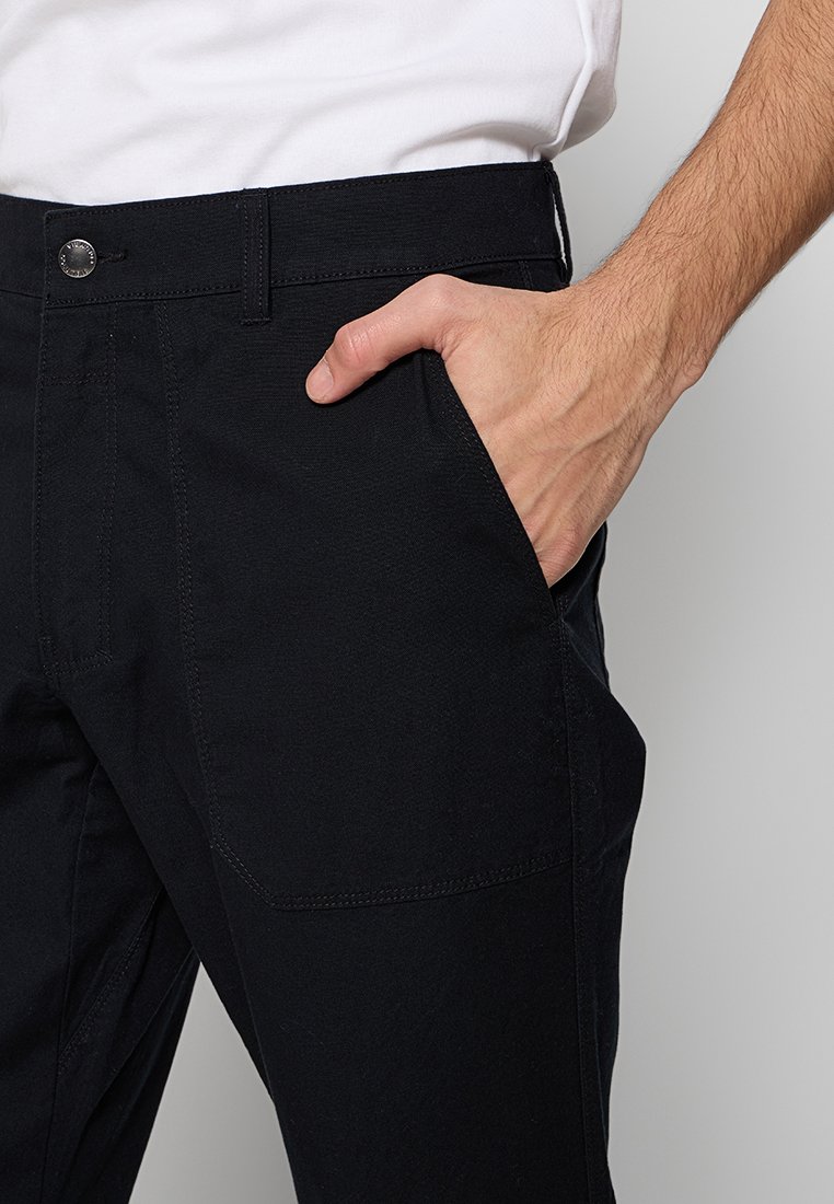 Schwarze Hose mit strukturiertem Finish, ausgestattet mit seitlichen Taschen und einem Metallknopfverschluss an der Taille. Die Passform ist tailliert und betont die Silhouette.
