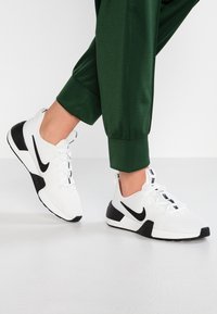 Valkoiset urheilukengät mustilla yksityiskohdilla, verkkokangasta yläsivussa, pehmeä pohja ja erottuva brändäys kielessä ja nauhoissa. Näkyvät tekstuuriset yksityiskohdat.