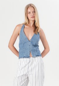 Denim-halteritoppi, jossa on syvä V-kaula-aukko, avoimet sivut ja etusivu. Vaaleansininen väri klassisella denim-textuurilla. Yhdistetty raidallisiin housuihin.
