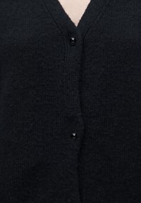 Gros plan sur un cardigan noir duveteux avec deux boutons noirs brillants fermés, montrant un tissu tricoté texturé et un décolleté en V.