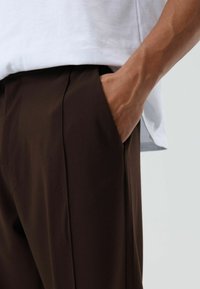 Bruine broek met een gladde textuur, voorzien van zijzakken en een getailleerde pasvorm, gedragen met een wit T-shirt.