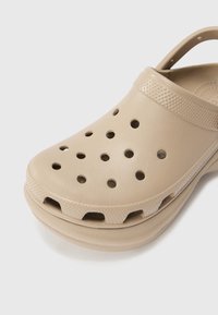 Sabot beige à enfiler avec des trous de ventilation, un bord de bride texturé et un bout arrondi, fabriqué en caoutchouc léger.