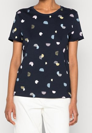 Marineblauw T-shirt met korte mouwen en ronde hals, versierd met verspreide pastelkleurige en witte halve cirkelpatronen, gedragen met een witte broek.