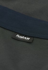 Tmavě šedé tričko s námořnickým vroubkovaným límcem. Obsahuje černou etiketu s bílým textem, který zobrazuje "IUMAN intimo uomo." Materiál z bavlněné směsi.