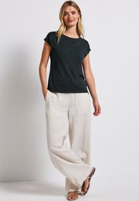 Zwart kortemouwtop met een V-hals, gecombineerd met lichtbeige, losse linnen broek en sandaaltjes met bandjes. Eenvoudig en ontspannen ontwerp.