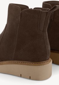 Bottes cheville en daim marron avec semelles épaisses en caoutchouc beige, fermeture éclair latérale, panneau élastique et languette à l'arrière.
