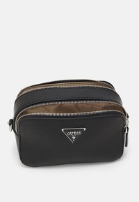 Černá texturovaná obdélníková crossbody taška se dvěma zipovými přihrádkami a stříbrným trojúhelníkovým logem Guess na přední kapse.