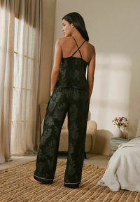 Musta kukkakuosiset pyjamat, joissa on löysä tanktoppi, jossa on säädettävät hihnat, ja leveät housut, joissa on kontrastivärinen reuna.