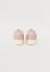 Zapatillas Nike en un suave tono rosa con un acabado de cuero liso, que presentan un logo blanco en el talón y una suela de goma texturizada.