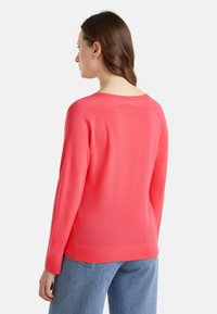 Maglione a maglia corallo con maniche lunghe, design raglan e ampio scollo. Tessuto liscio e dettaglio a coste sull'orlo. Indossato con denim chiaro.