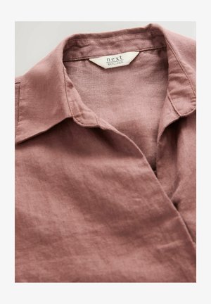 Linen shirt in dusty pink with a classic collar. Features a subtle texture and a label indicating it's 100% linen.