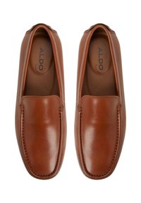 Zapatos slip-on de cuero marrón con un acabado suave, puntera redondeada y costuras visibles alrededor de los bordes. La marca está grabada en la plantilla.