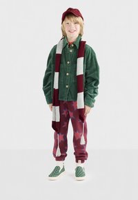 Παιδί με πράσινο πουκαμισάκι κοτλέ, μπορντό παντελόνι με αστέρια, ριγέ κασκόλ και πράσινα παπούτσια τύπου slip-on με πουά, φορούσε και καπέλο.