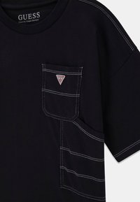 Czarny t-shirt o klasycznym kroju, z kieszonką na piersi z naszywką z logo, kontrastującym białym przeszyciem i okrągłym dekoltem.